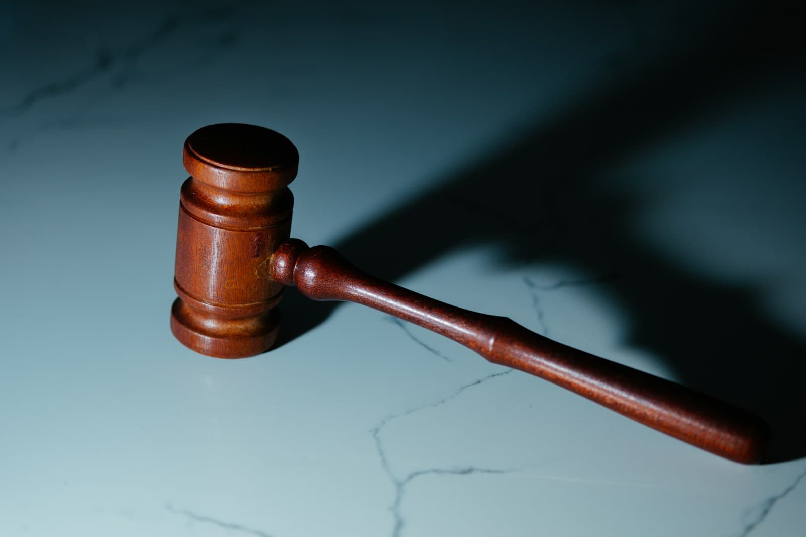 Wooden judge's gavel casting shadow on marble surface with blue-gray background
