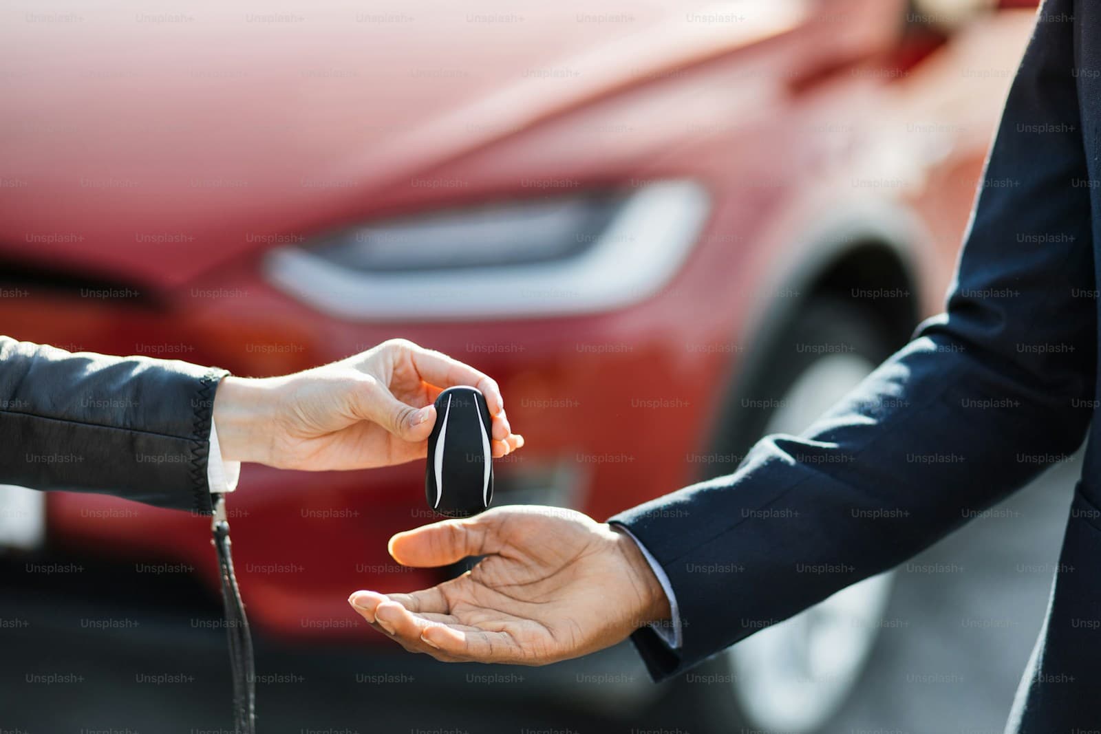 Two people exchanging car keys with a red car in the background